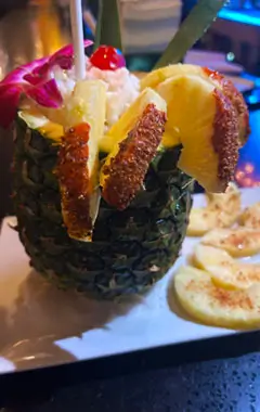 A whole pineapple with a slice placed on top, showcasing its vibrant green leaves and textured yellow skin.