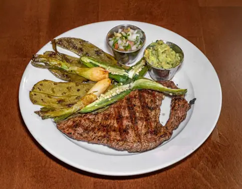 A plate featuring a grilled steak, colorful vegetables, and a side dish, arranged appetizingly.