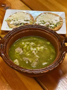 A bowl of steaming soup accompanied by a plate of warm tortillas on a wooden table.