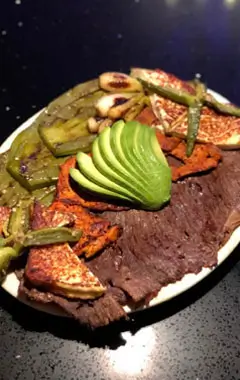 A plate featuring a serving of meat, assorted vegetables, and sliced avocado arranged artfully.